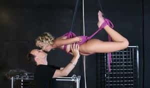 Blonde chick is suspended by purple ropes and made to suck cock