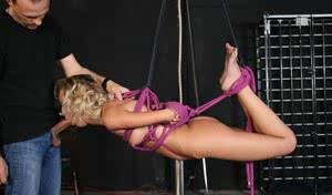 Blonde chick is suspended by purple ropes and made to suck cock