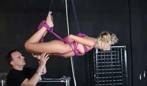 Blonde chick is suspended by purple ropes and made to suck cock